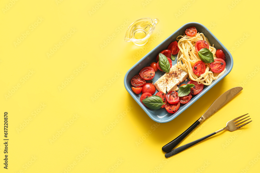 Baking dish of tasty pasta with tomatoes and feta cheese on yellow background