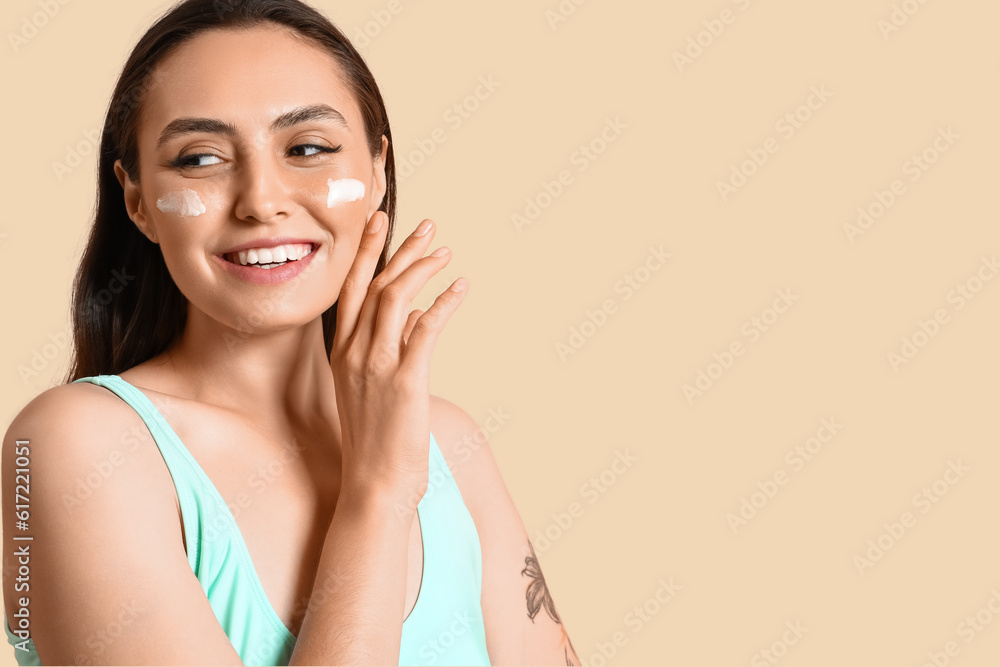 Young woman with sunscreen cream on beige background, closeup