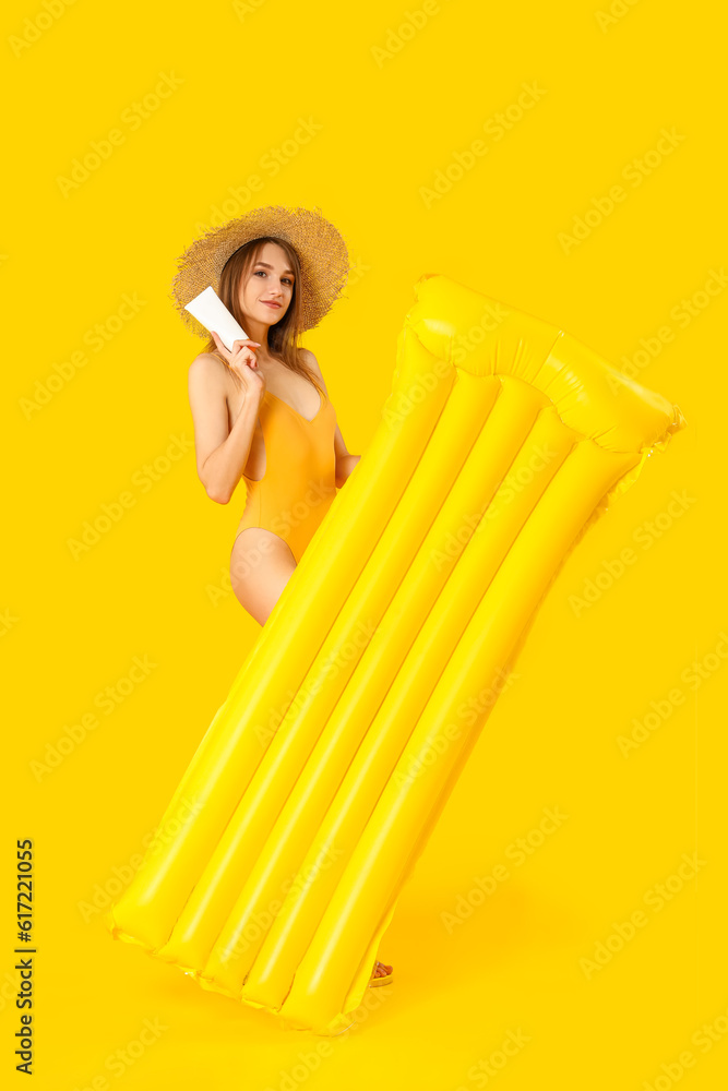 Young woman with sunscreen cream and inflatable mattress on yellow background