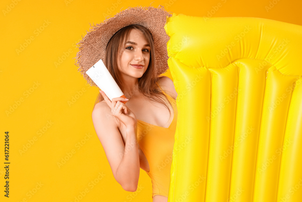 Young woman with sunscreen cream and inflatable mattress on yellow background