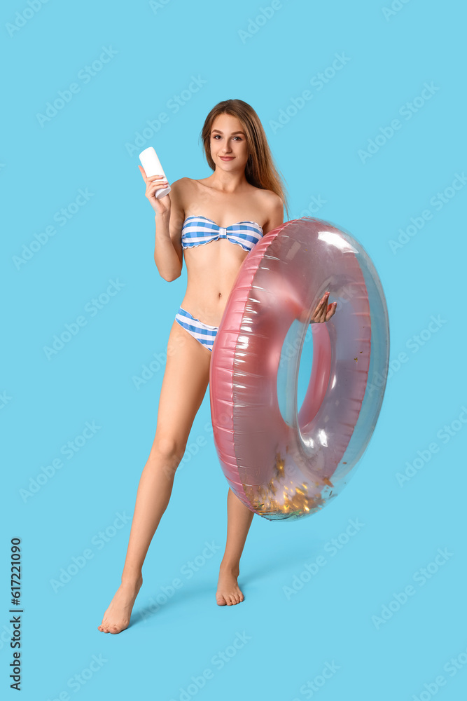 Young woman with sunscreen cream and inflatable ring on blue background