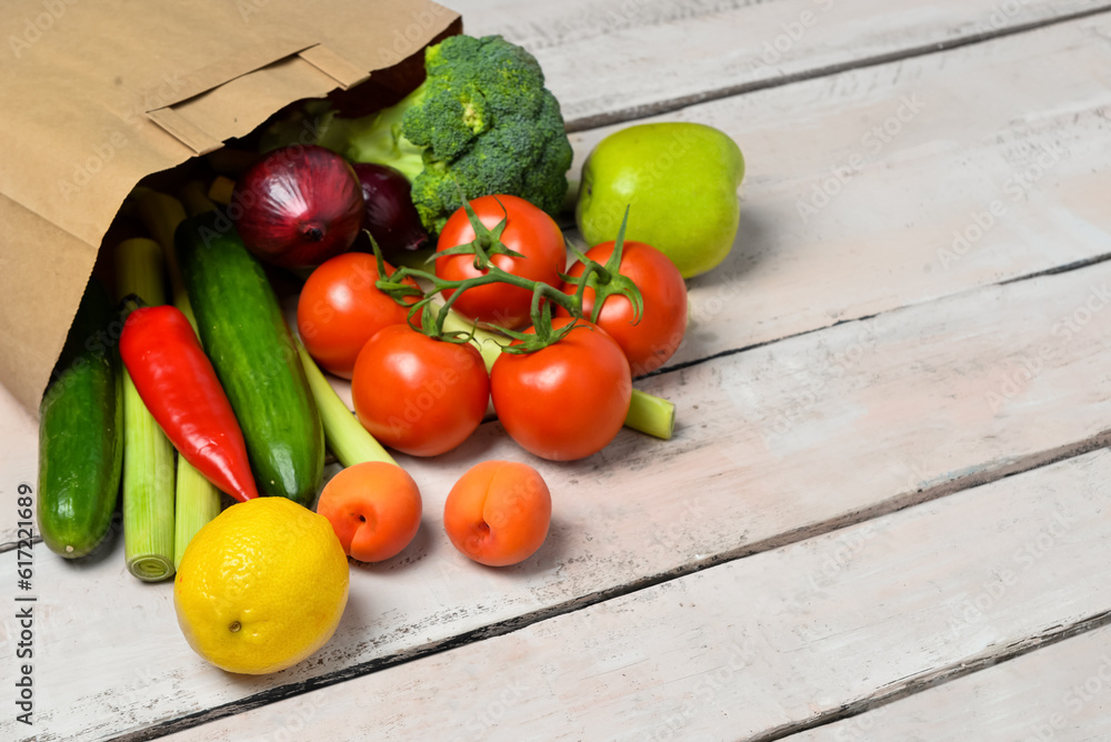 Paper bag with fresh vegetables and fruits on light wooden background