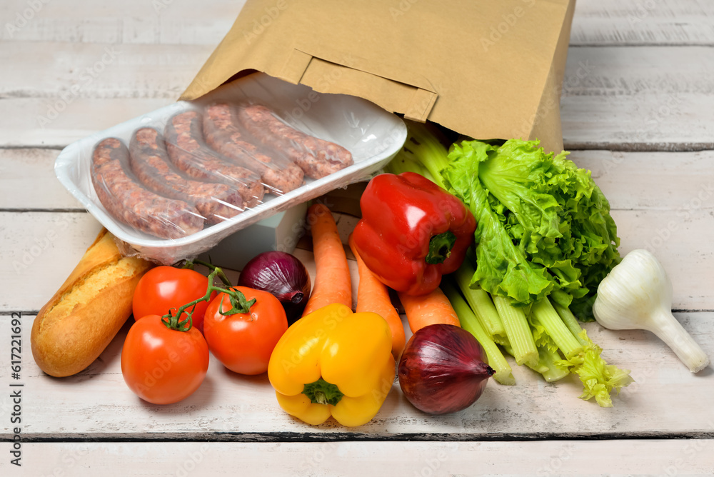 Paper bag with different products on light wooden background