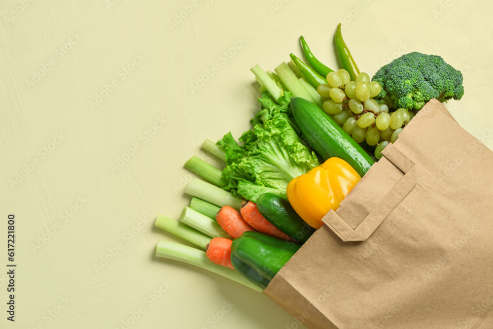 Paper bag with fresh vegetables and fruits on beige background