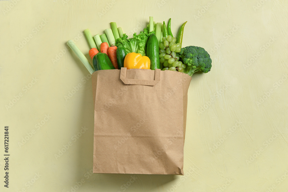 Paper bag with fresh vegetables and fruits on beige background