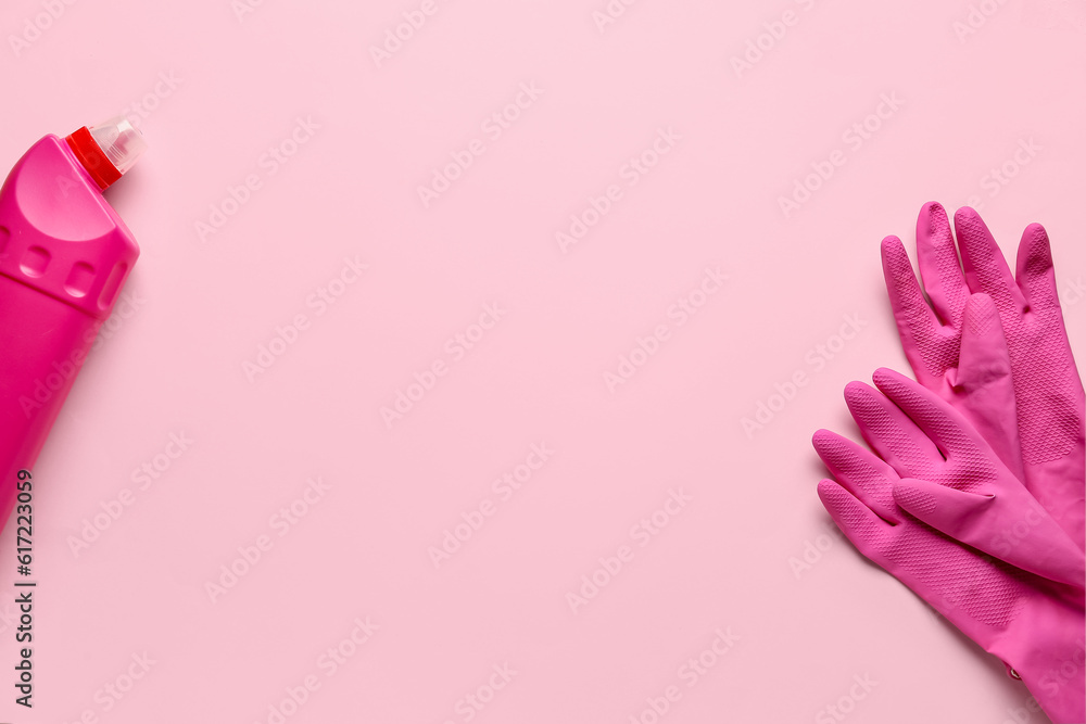 Pair of protective rubber gloves and bottle of detergent on pink background