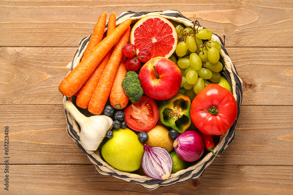 Wicker bowl with different fresh fruits and vegetables on wooden background