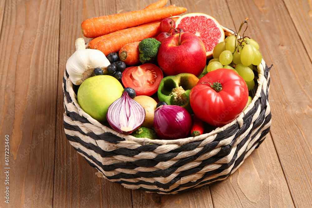 Wicker bowl with different fresh fruits and vegetables on wooden background