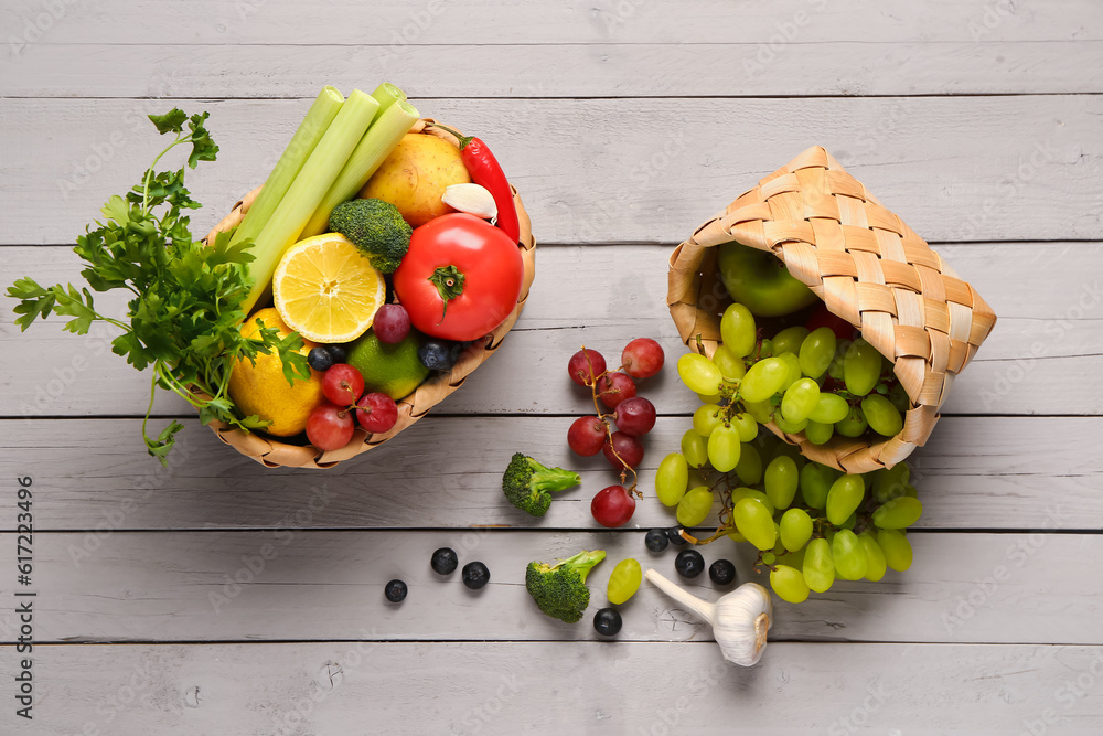 Wicker baskets with different fresh fruits and vegetables on grey wooden background