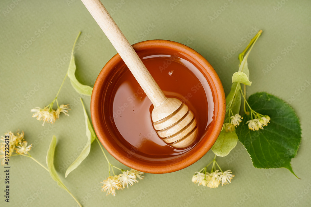 Bowl with linden honey and dipper on green background