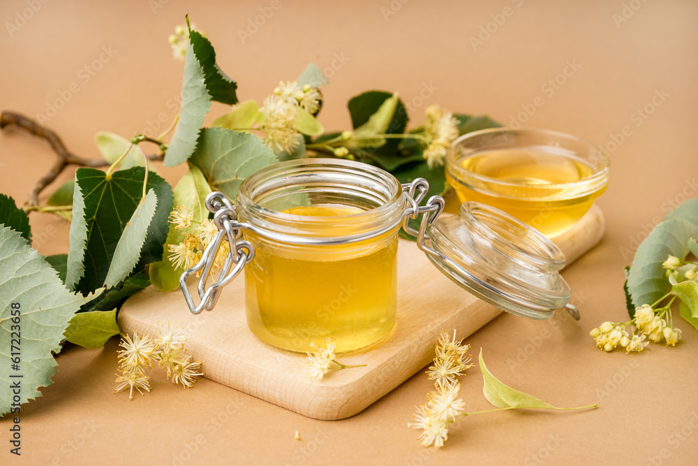 Wooden board with jar and glass bowl of linden honey on brown background