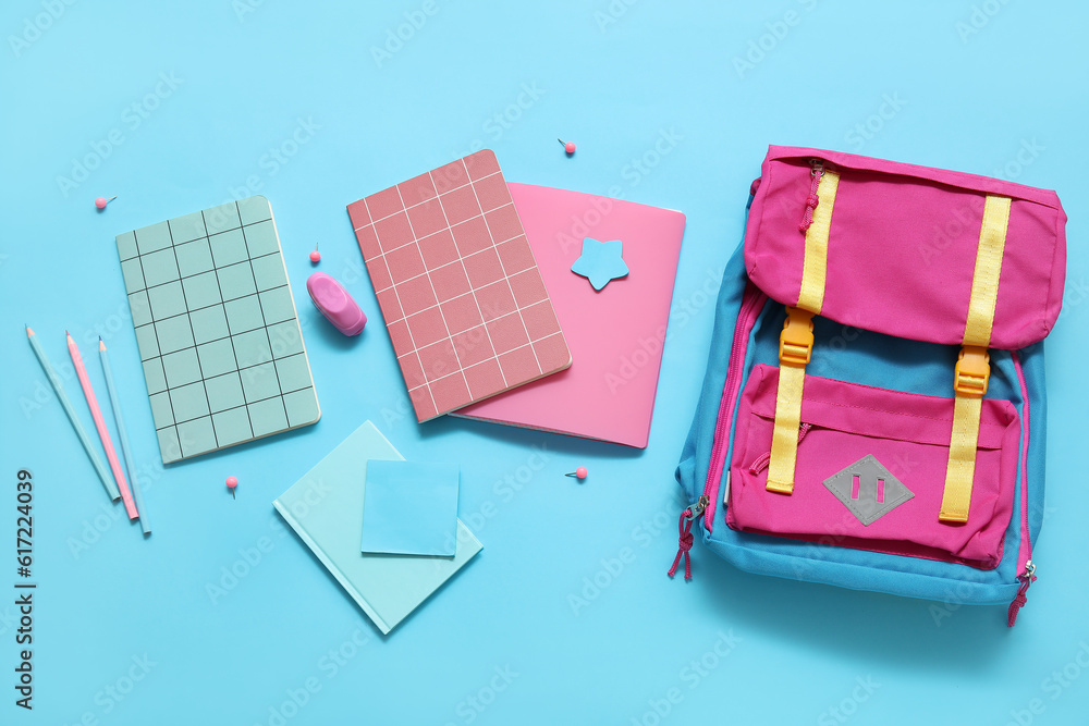 Colorful school backpack with notebooks, pencils and stapler on blue background