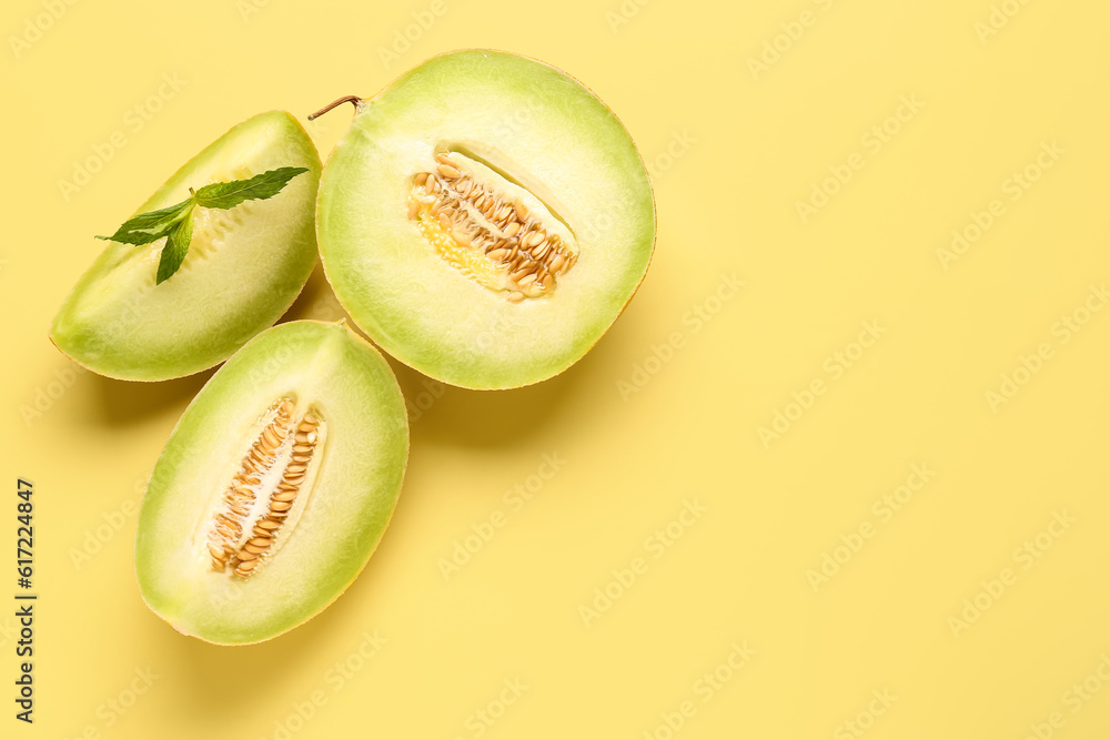 Half of sweet melon with pieces and mint on yellow background