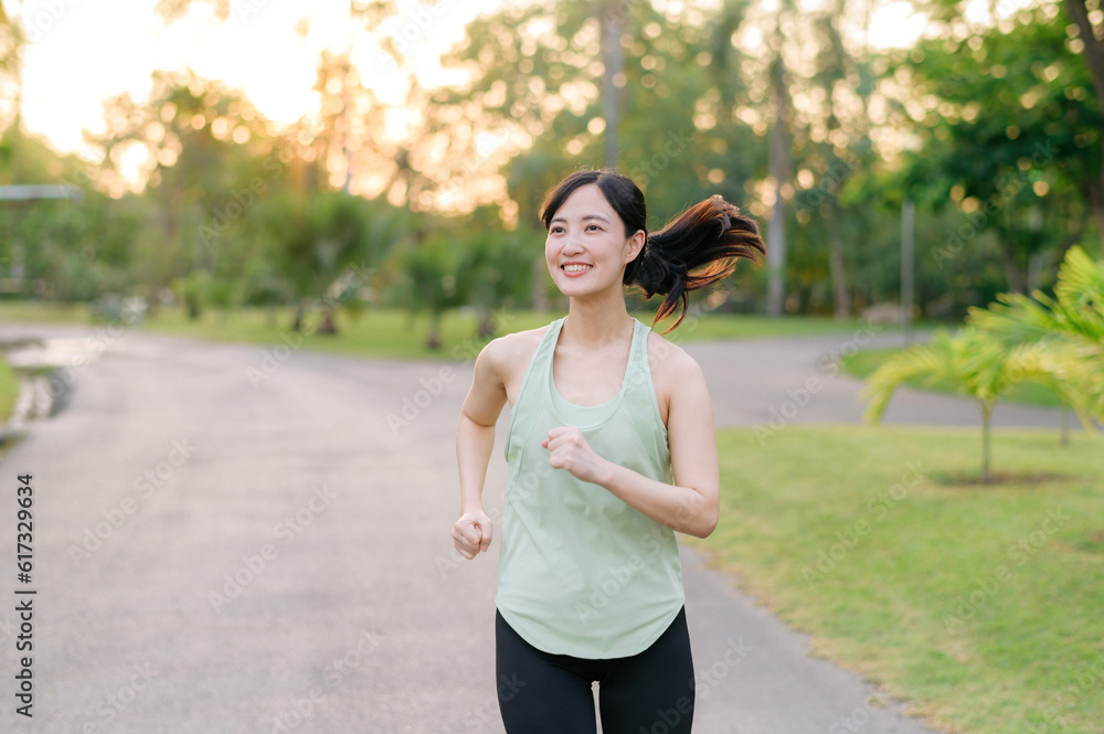 Fit Asian young woman jogging in park smiling happy running and enjoying a healthy outdoor lifestyle