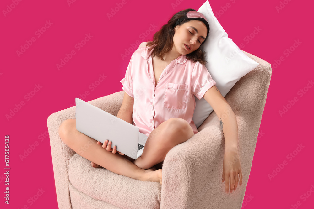 Young woman with laptop sleeping in armchair on pink background