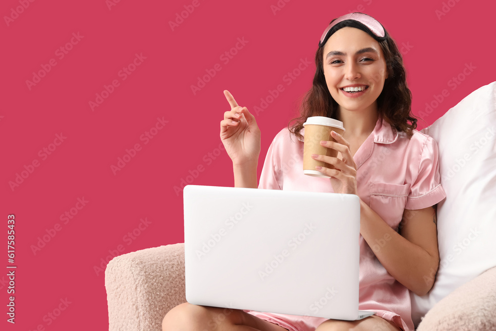 Young woman with cup of coffee and laptop pointing at something on pink background