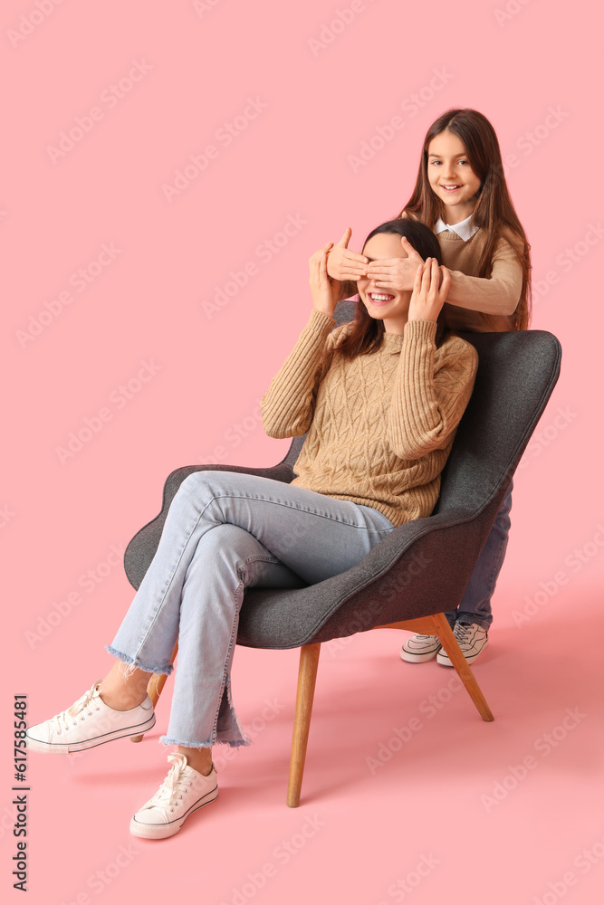 Little girl closing her mothers eyes on pink background