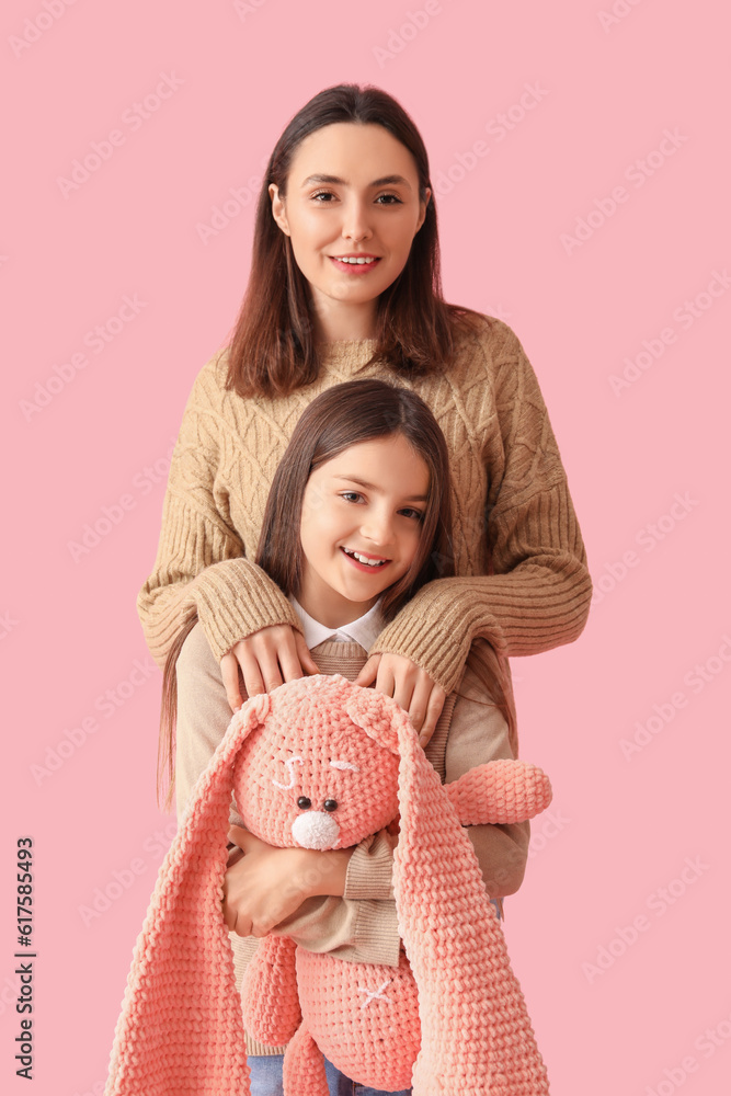 Little girl and her mother in warm sweaters with toy bunny on pink background