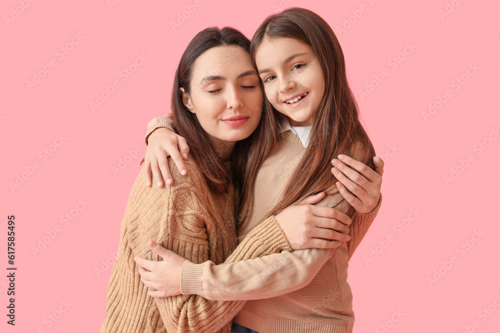 Little girl and her mother in knitted sweaters hugging on pink background