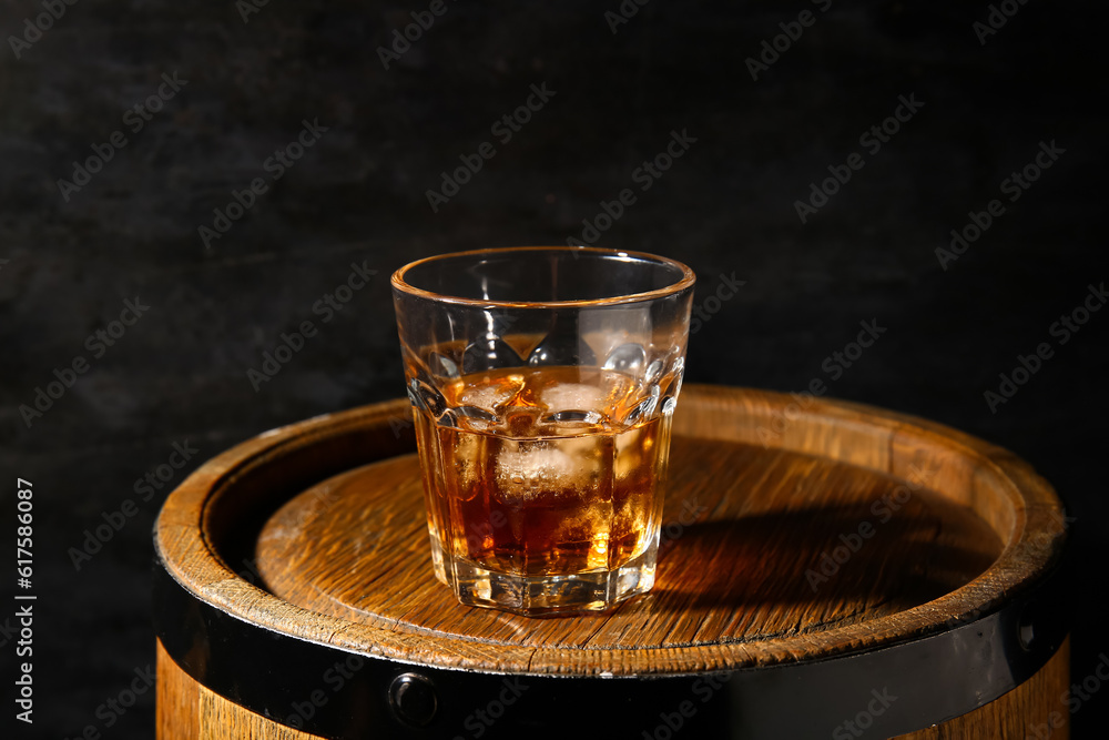 Barrel with glass of cold rum on black background