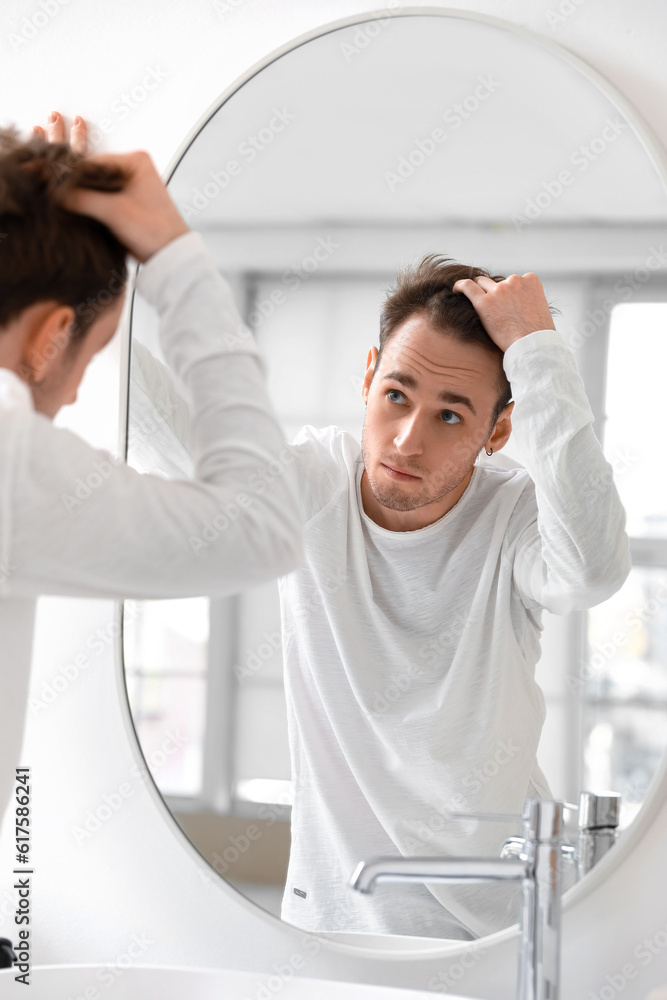 Young man with hair loss problem looking in mirror at home