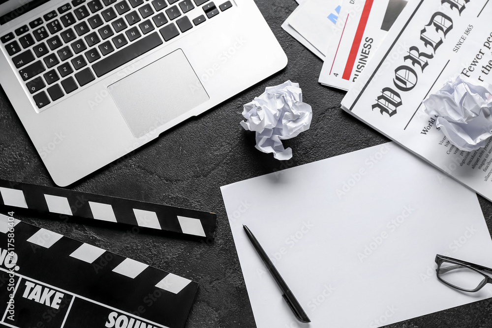 Paper sheet with movie clapper, newspapers and laptop on dark background