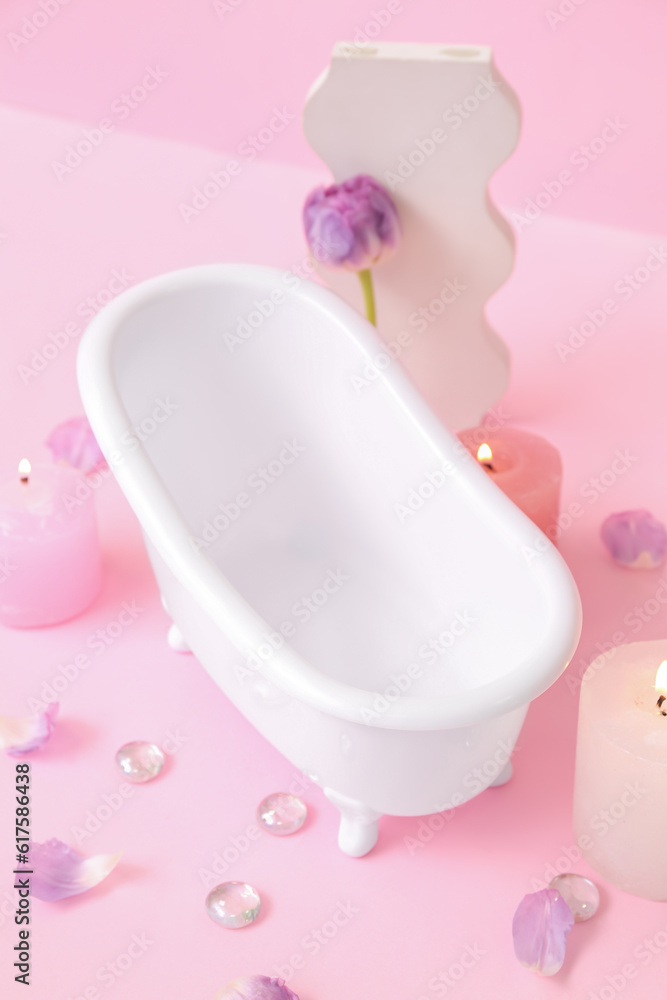 Small bathtub, burning candles and decor on pink background