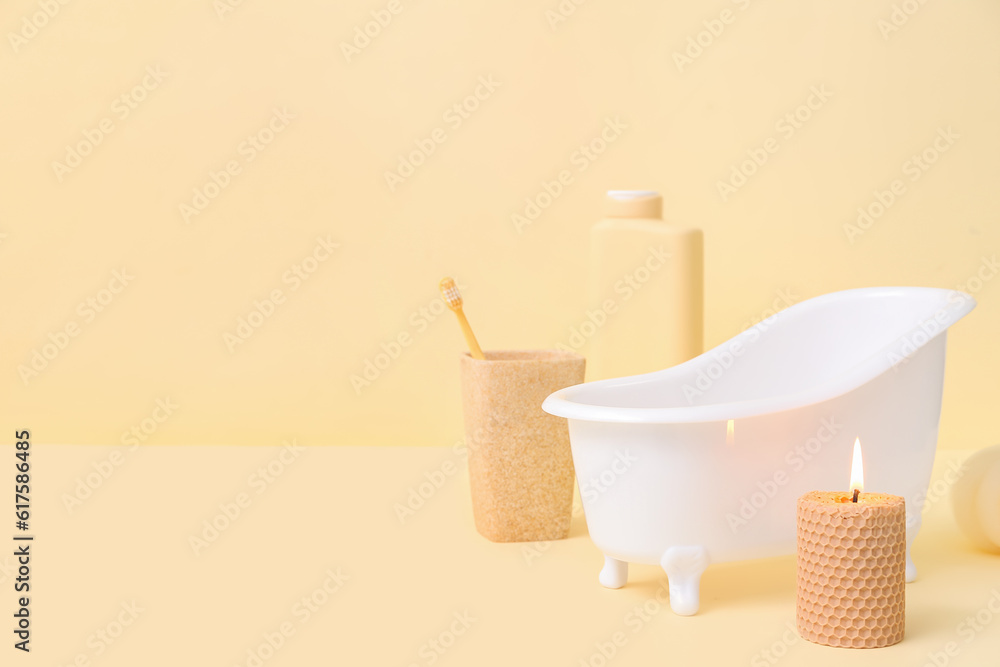 Small bathtub, burning candle and bath supplies on color background