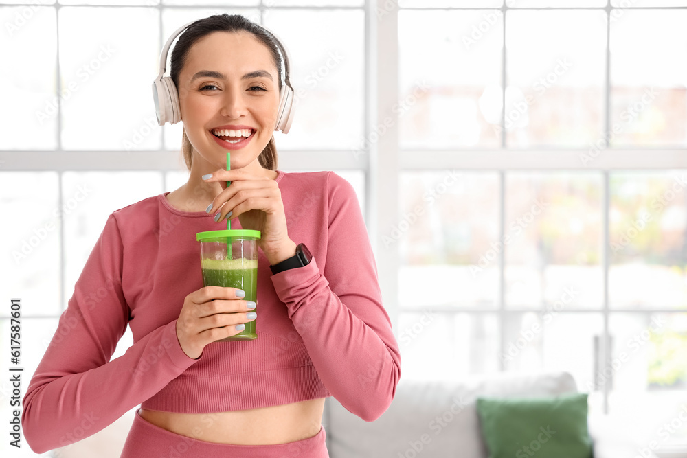 Sporty young woman in headphones with glass of vegetable juice at home