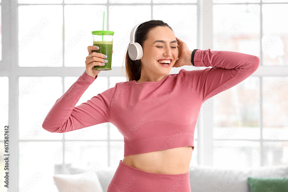 Sporty young woman in headphones with glass of vegetable juice at home