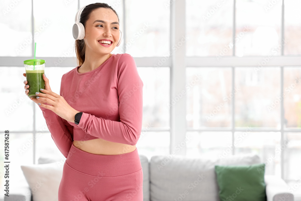 Sporty young woman in headphones with glass of vegetable juice at home