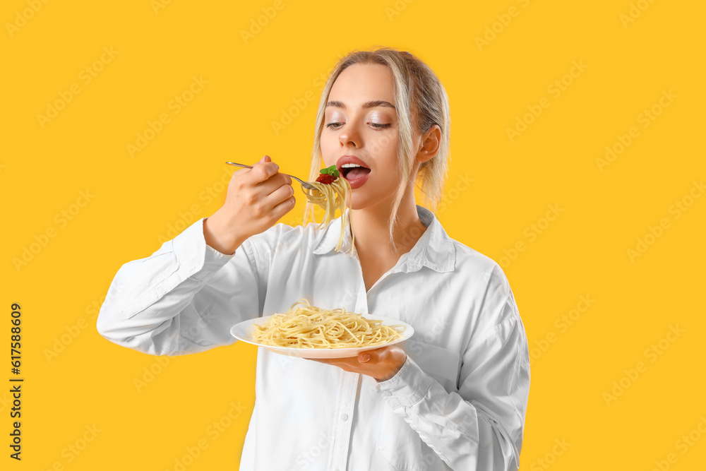 Young woman eating tasty pasta on yellow background