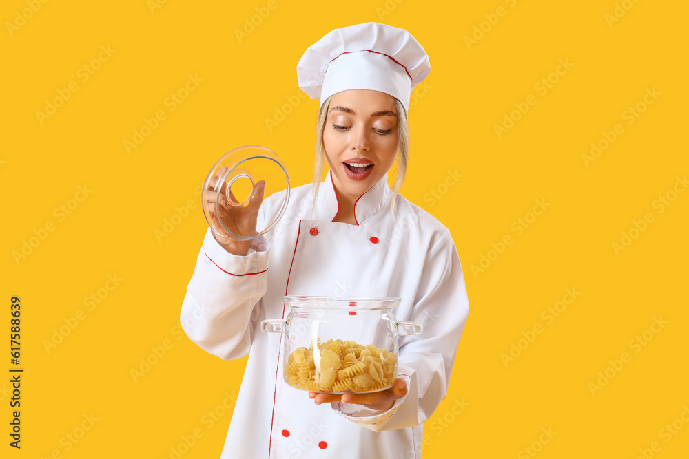 Female chef with cooking pot of pasta on yellow background