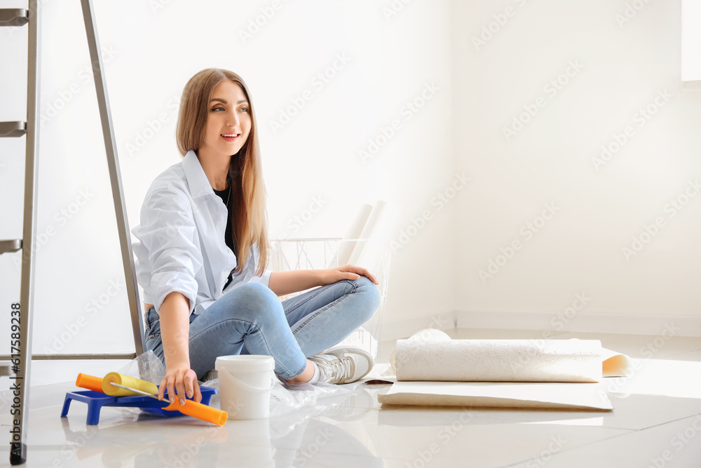 Young woman with supplies and wallpaper rolls in room