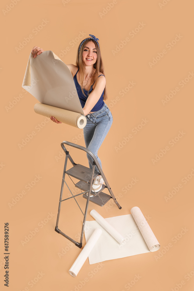 Young woman with wallpaper roll on ladder against beige background