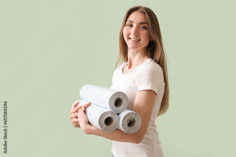 Young woman with wallpaper rolls on green background