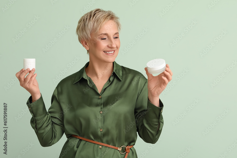 Mature woman with jars of cream on green background