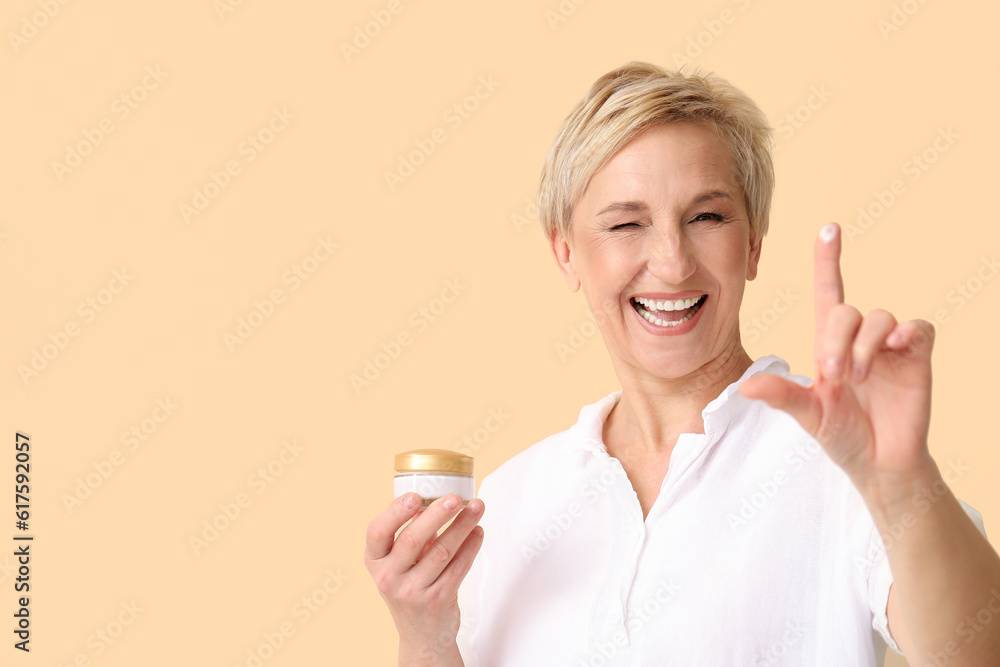 Mature woman with jar of cream on beige background