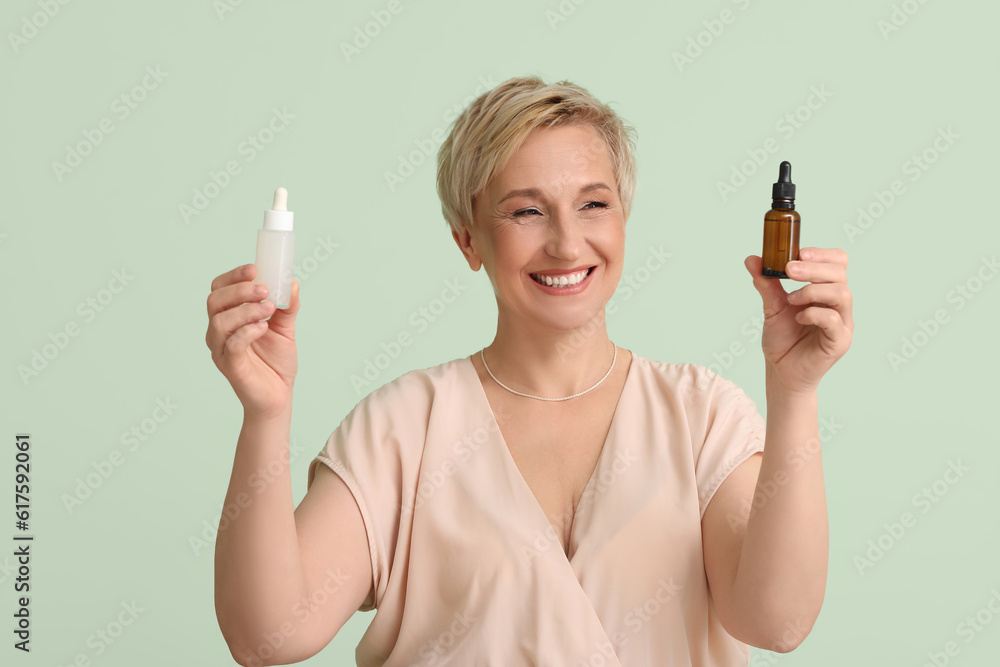 Mature woman with bottles of serum on green background