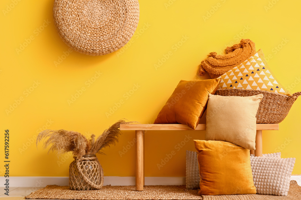 Basket with stylish pillows on bench near yellow wall in room