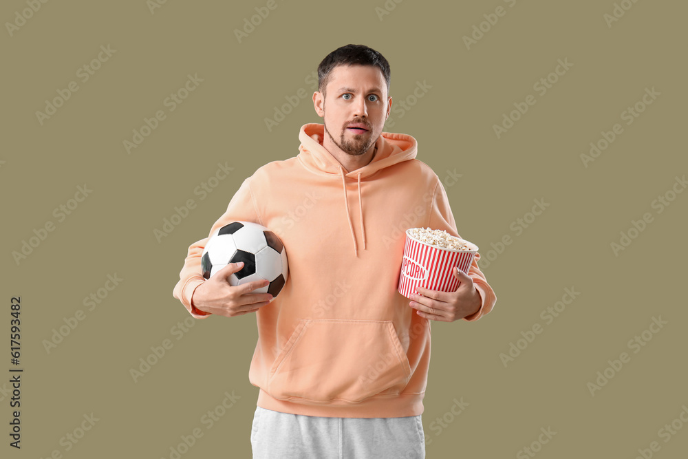 Soccer fan with ball and popcorn on color background