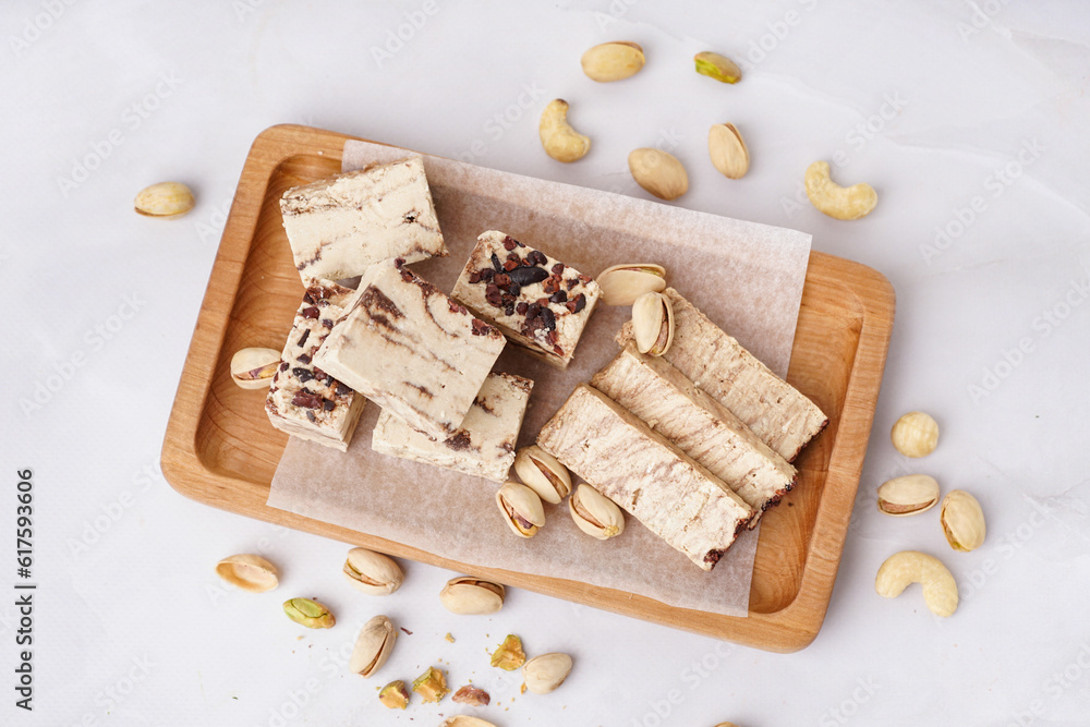 Wooden board with pieces of tasty marble halva on light background