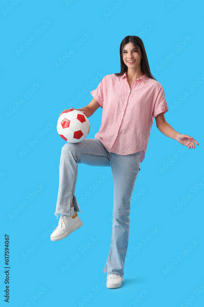 Young woman playing with soccer ball on blue background