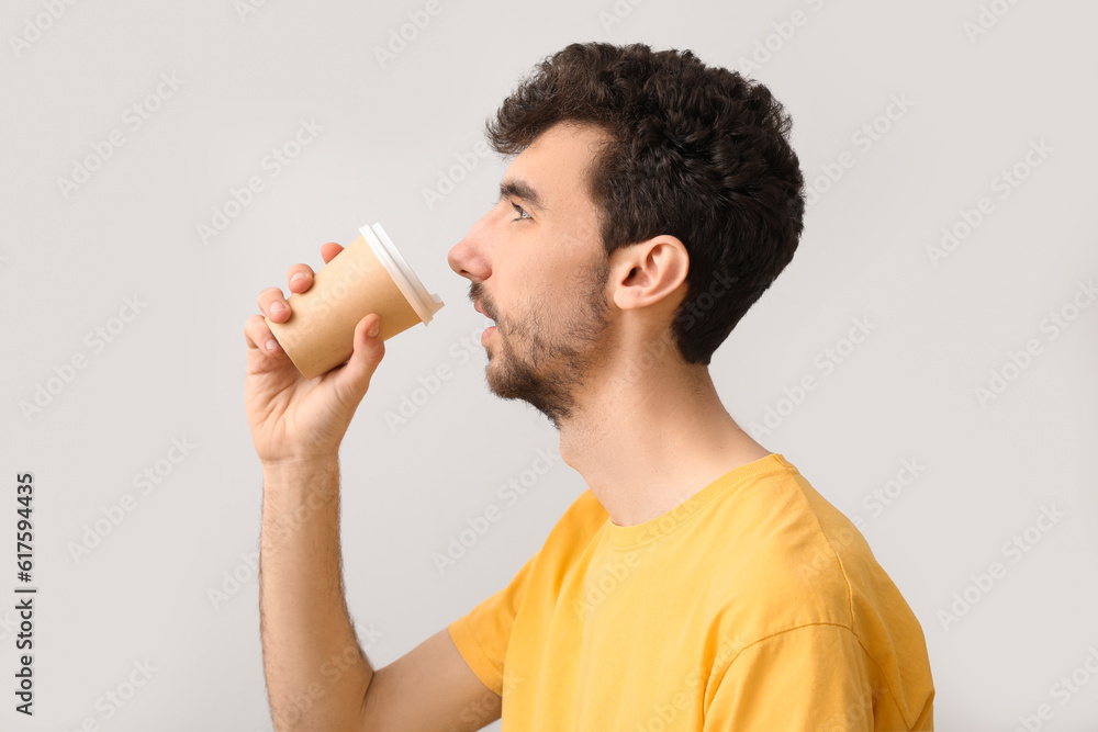 Young brunette man with cup of coffee on light background