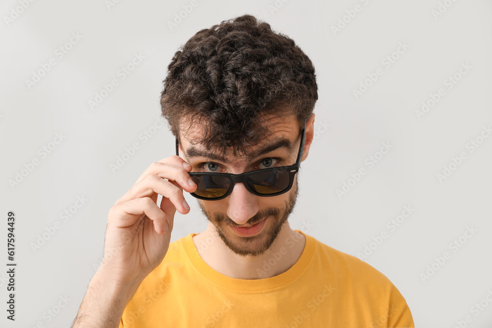 Young brunette man in sunglasses on light background, closeup