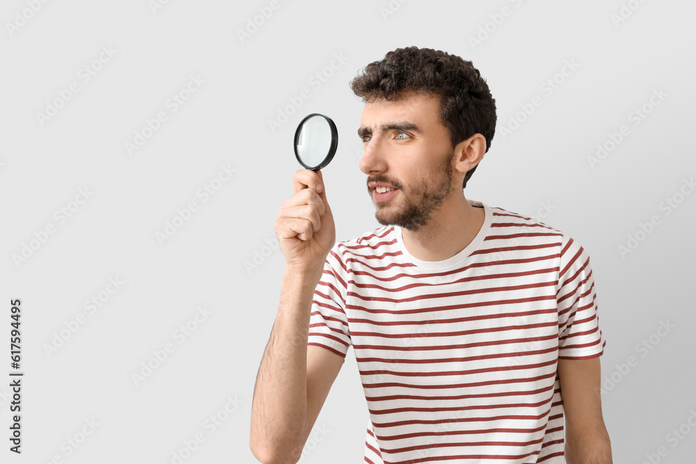 Young man with magnifier on light background