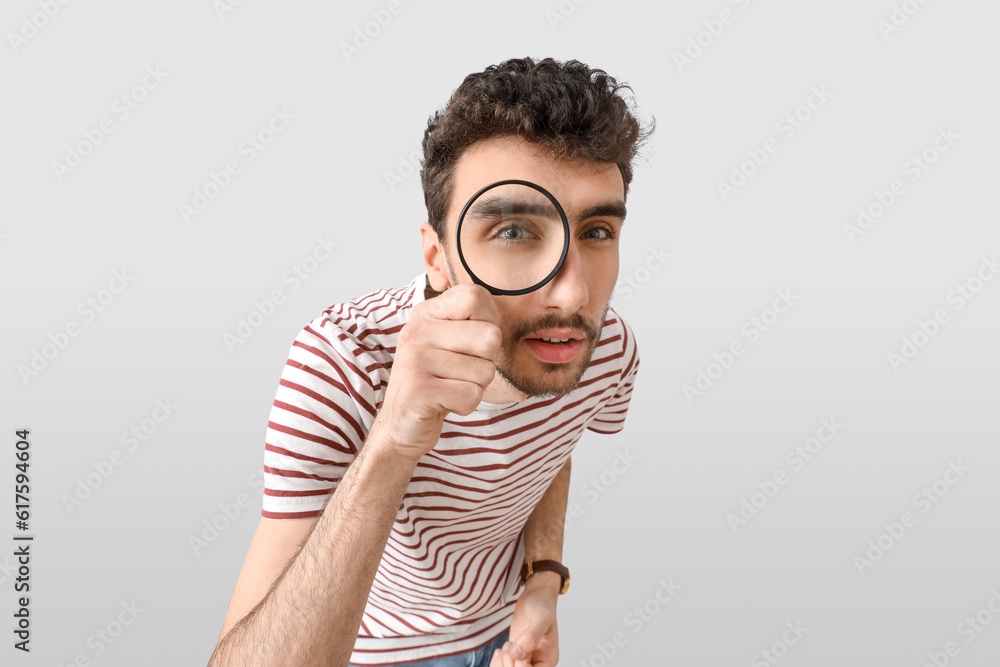 Young man looking through magnifier on light background, closeup