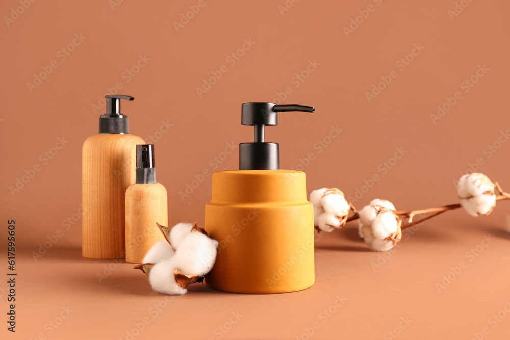 Bottles of cosmetic products with cotton flowers on color background