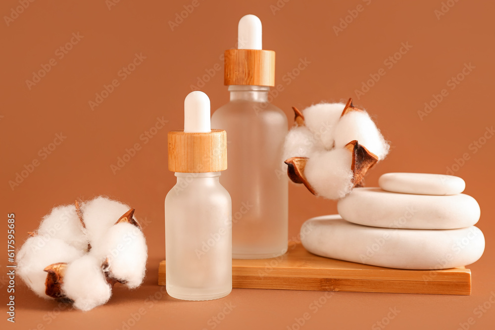 Bottles of essential oil, cotton flowers and spa stones on color background