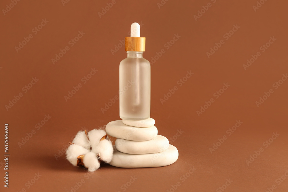 Bottle of essential oil, spa stones and cotton flower on color background